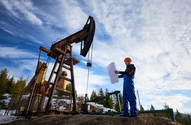 Oil worker standing by oil well pump jack