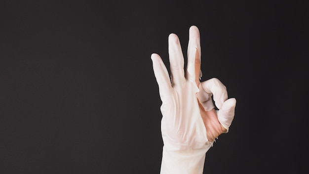 Ok hand sign and wear latex glove on black background