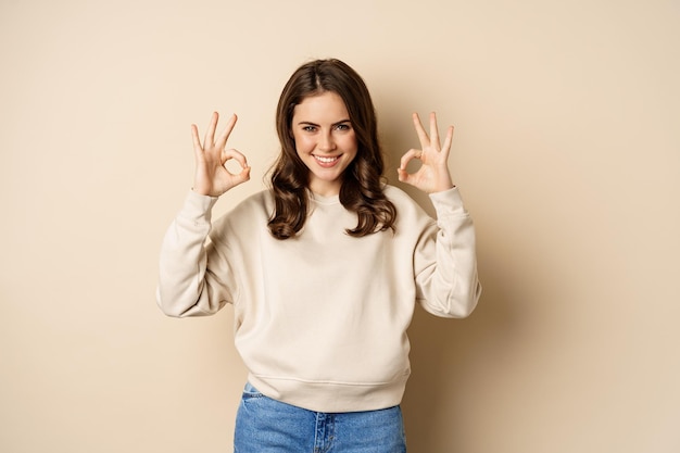 Okay confident smiling modern girl showing ok sign approve like and recommend smth good standing ove...