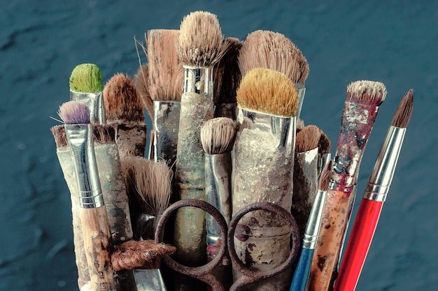 Old art brushes stand on the blue wall of a colored wall in the artist's studio