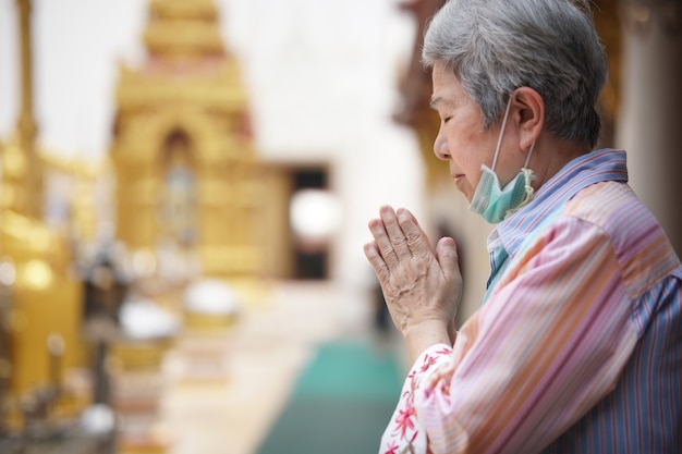 Old asian elder senior woman traveler tourist praying at buddhist temple.