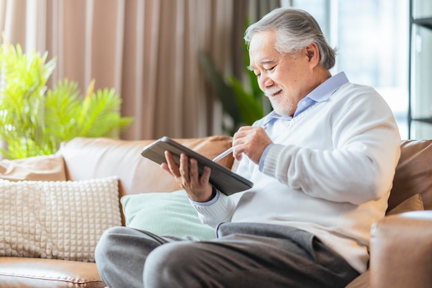 Old asian senior grandfather enjoy sunday weekend reading notebook on sofa couch at homehome isolation senior male adult relax casual happiness at home