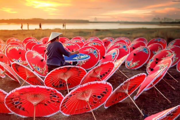 An old Asian woman is painting a colorful gathering by the lake at sunset.