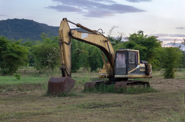 Old backhoe on construction site in the green fields with sunset