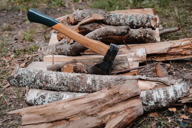 An old battered axe is stuck in a log on a pile of firewood Outdoor recreation Preparation for the bonfire