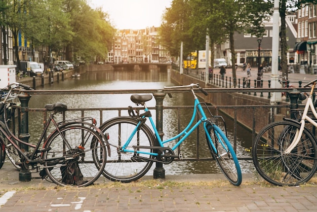 Old bicycle on the bridge in Amsterdam Netherlands against a canal during summer sunny day Postcard iconic view Tourism concept