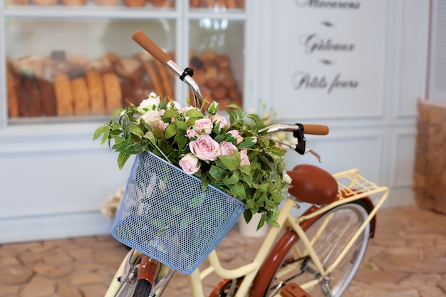 old bicycle with a basket of roses against the wall in pastel colors. Decorative bicycle stand for plants and flowers. 