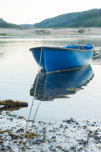 Old blue boat on the water against the backdrop of the mountains Beautiful harsh northern nature Vertical