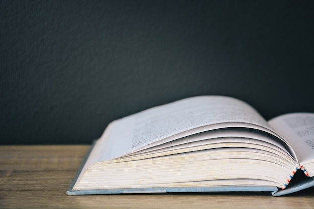 An old book open on a wooden table with black color wall background and light from above