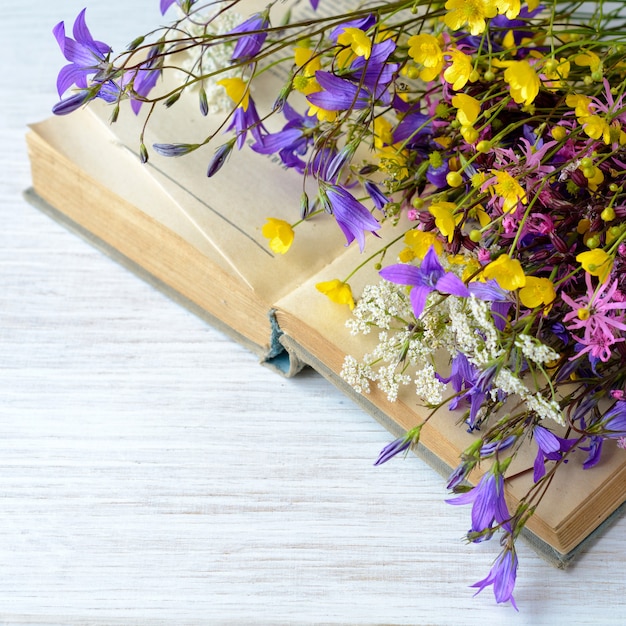 Old book with bouquet of meadow flowers nostalgic vintage background