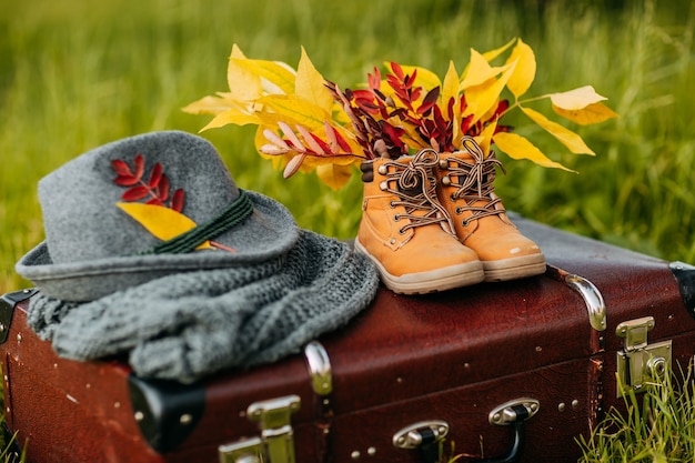 Old boots, felt hat and knitted scarf on the brown vintage suitcase in autumn forest