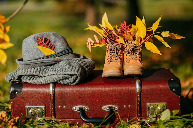 Old boots, felt hat and knitted scarf on the brown vintage suitcase in autumn forest