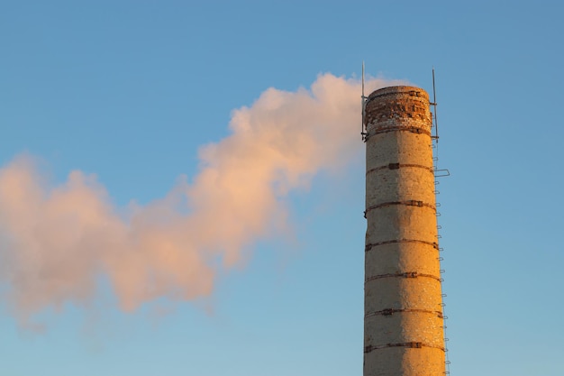 an old brick chimney of a factory boiler room with smoke on a blue sky background