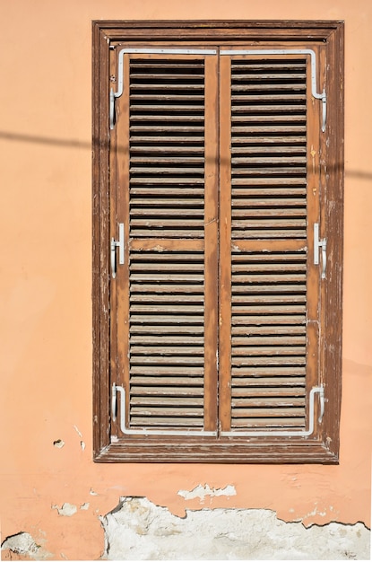 Old brown wooden window with shutters and wall with cracked paint