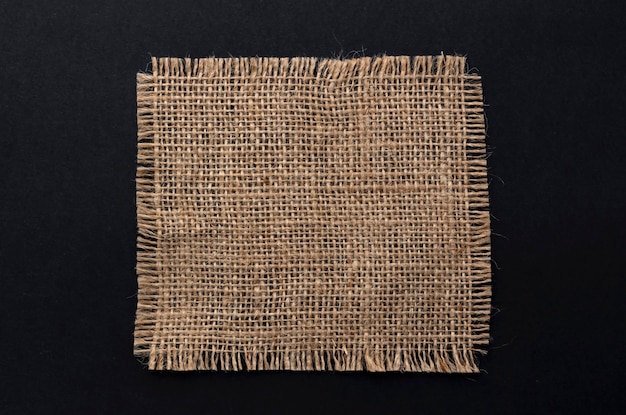 Old burlap fabric napkin on black background, top view