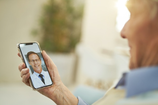 Old caucasian man looking at smartphone and chatting online with a doctor