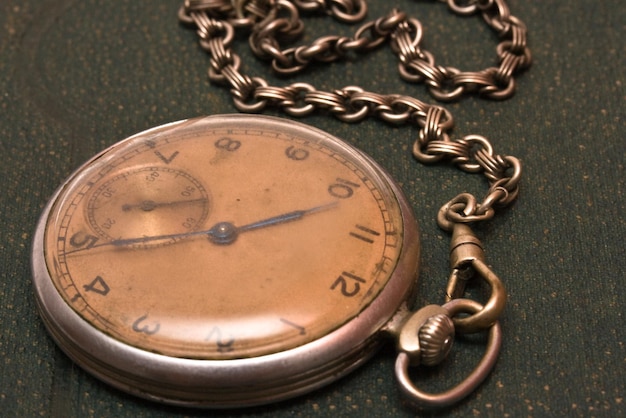 Old clock with chain lying on rough green surface