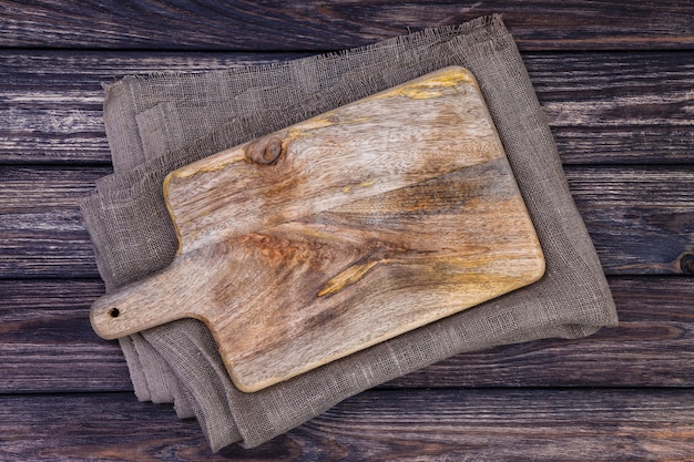 Old cutting board on dark wooden table. Top view. Copy space