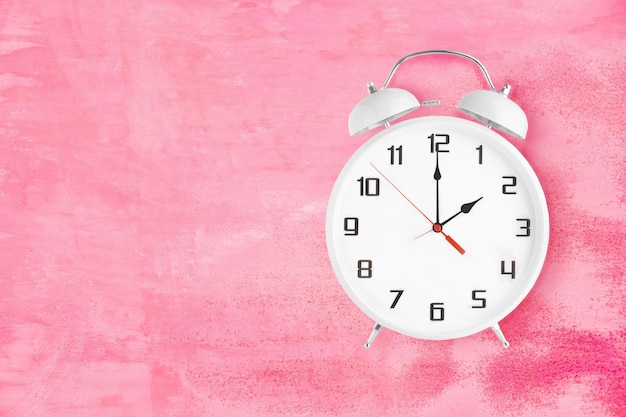 Old fashioned alarm clock with twin bells and ringer showing 2 o'clock on pink background