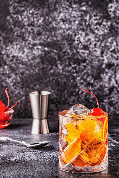 Old fashioned cocktail with cherries and orange twist, selective focus.