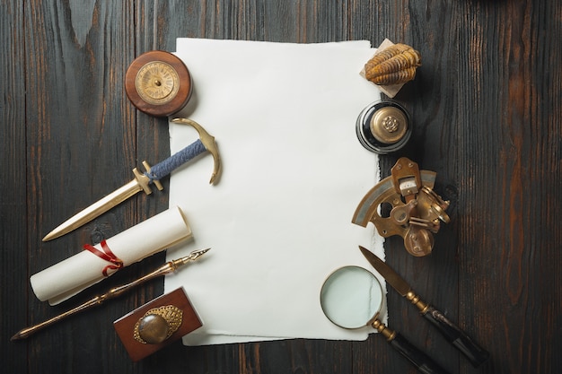 Old fashioned flat lay with letters writing accessories on dark wooden background. White sheets, pen, signet, package, ink. Vintage style, steampunk, gaslight concept. Magnifying glass and compass.