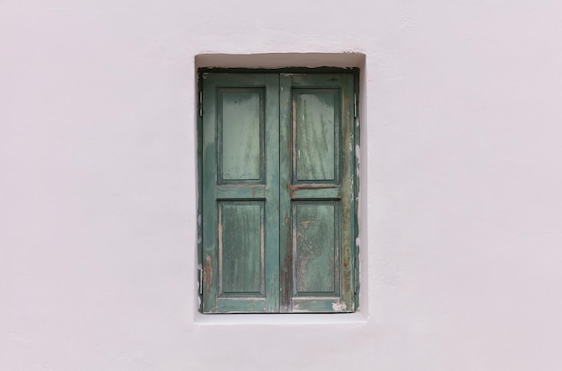 Old fashioned worn window with green wooden shutters closed on painted wall background