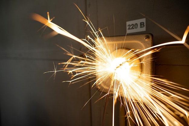 An old faulty outlet with a broken 220 volt power cord plugged in sparkles with bright electrical dangerous sparks and produces a short circuit