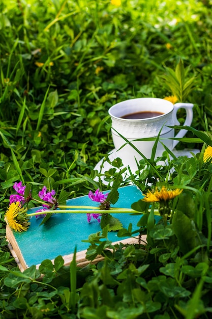 An old green book with wildflowers and a cup of coffee on a green meadow on a summer or spring morning