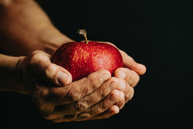 Old hands grabbing a red apple with water drops