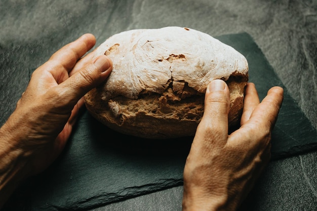 Old hands preparing freshly baked artisan and organic bread over a rustic table Homemade cooking Sourdough bread with crispy crust on wooden shelf Bakery goods concept Restaurant and goods