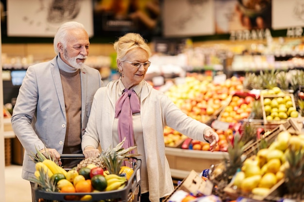 An old healthy couple is purchasing fresh fruits at the supermarket