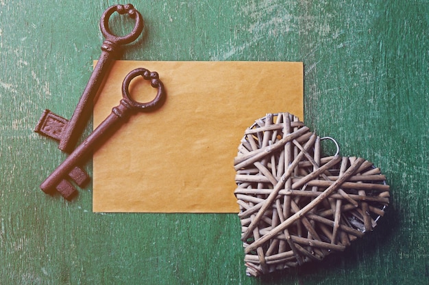 Old key with decorative heart and sheet of paper on green scratched wooden background close up