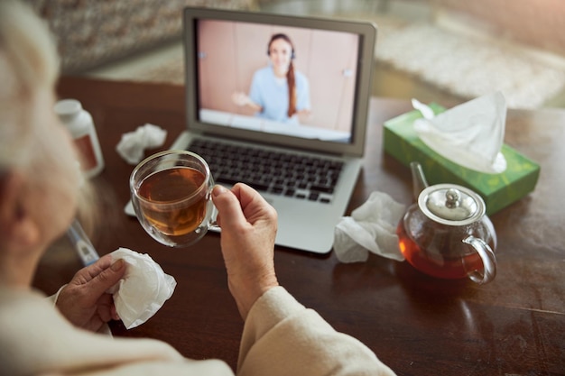 Old lady drinking tea and having online consultation with doctor