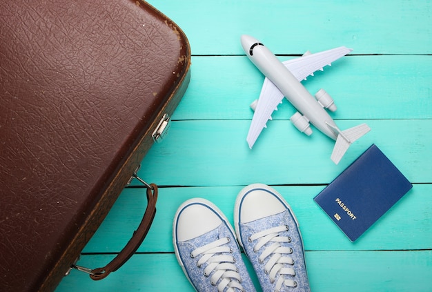 Old luggage, airplane figurine, passport, sneakers on blue wooden floor