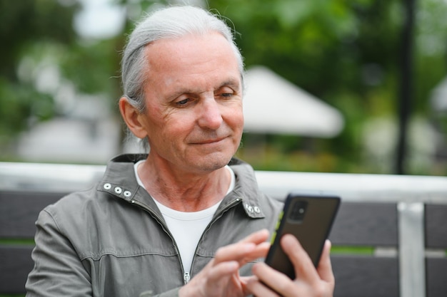 Old man browsing app on smartphone outdoor in park