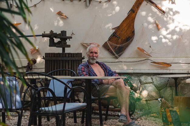 Photo an old man in a home plaid shirt sits at a table surrounded by fishing and vinery attributes an aged man farmer and fisher rests in his own villa