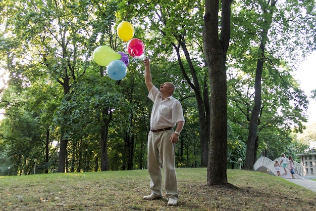 An old man is playing in the park with bright balloons on his birthday