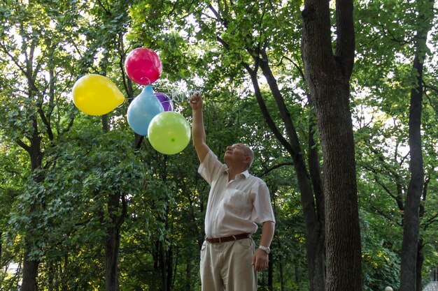 An old man is playing in the park with bright balloons on his birthday