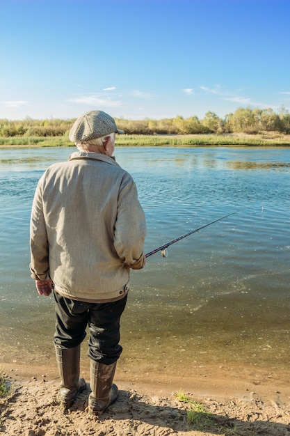 The old man is standing by the yard with a fishing rod