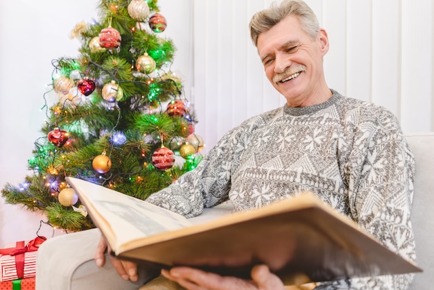 The old man look to a photo album near the christmas tree