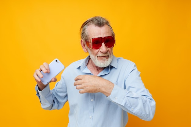 Old man posing emotions with phone in hand yellow background