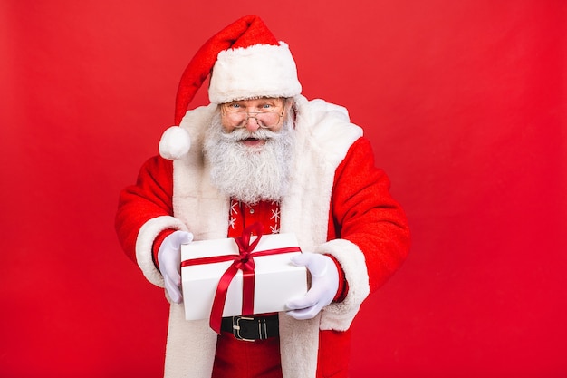 old man in Santa Claus costume holding a present isolated on red background