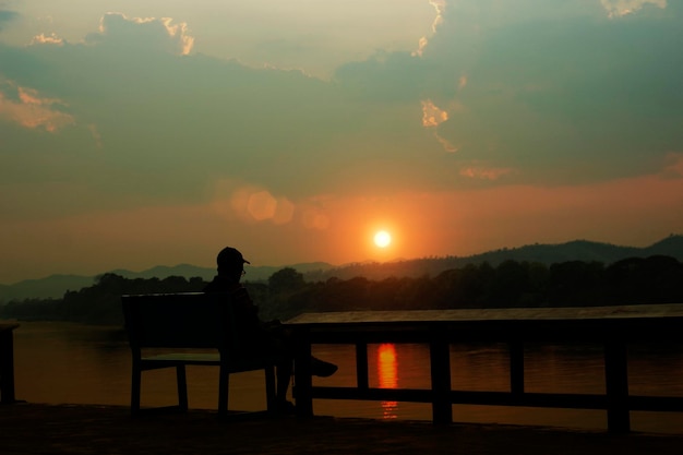 The old man sits at a bench near the river