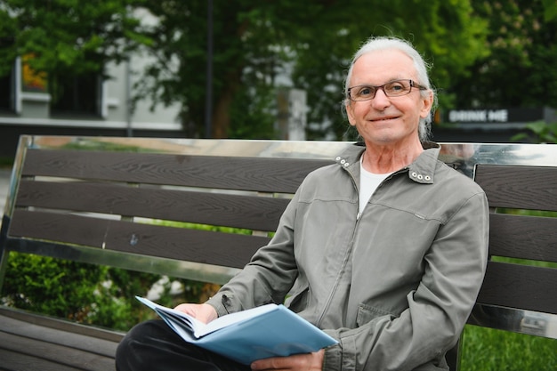 Old man with gray hair reads a book on a bench in the park Rest in the park