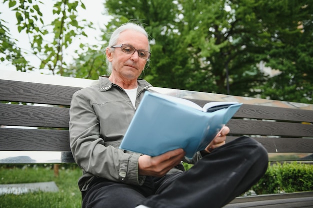 Old man with gray hair reads a book on a bench in the park Rest in the park