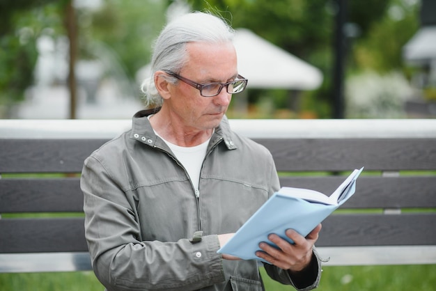 Old man with gray hair reads a book on a bench in the park Rest in the park