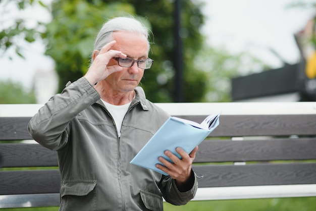 Old man with gray hair reads a book on a bench in the park Rest in the park