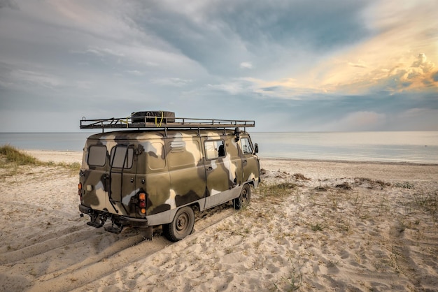 Old military car on the beach sand at sunset