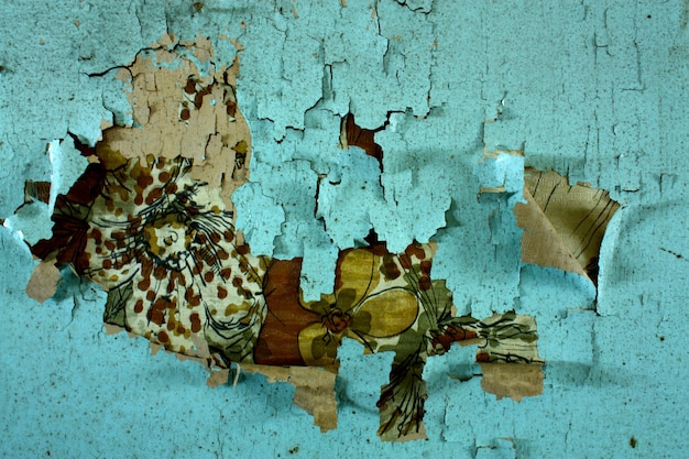 An old mural is revealed behind crumbling teal paint