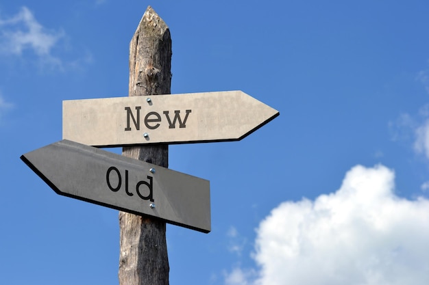 Old or new wooden signpost with two arrows sky with clouds